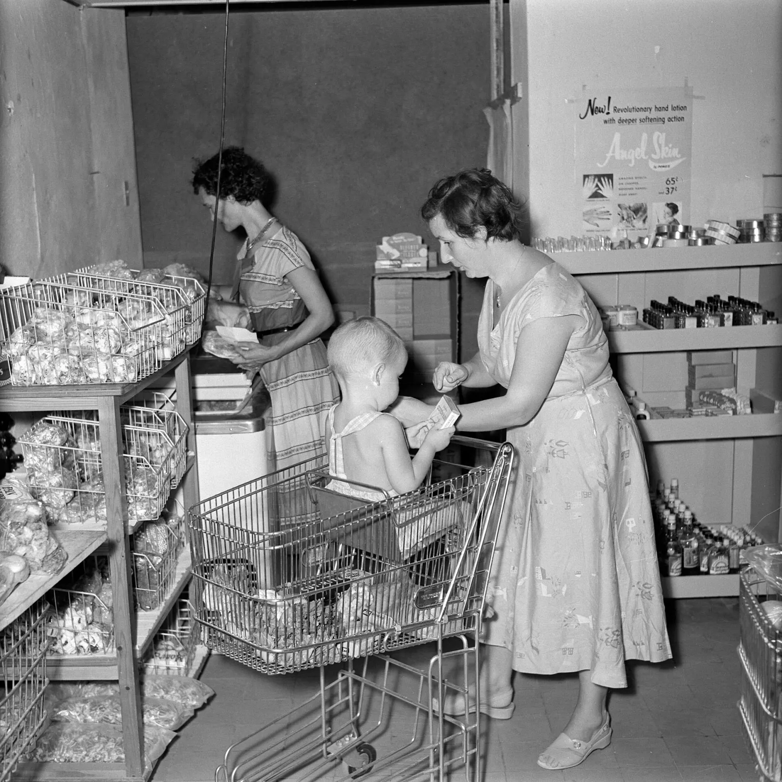 A woman with a child in a shopping trolley choosing goods in a supermarket aisle